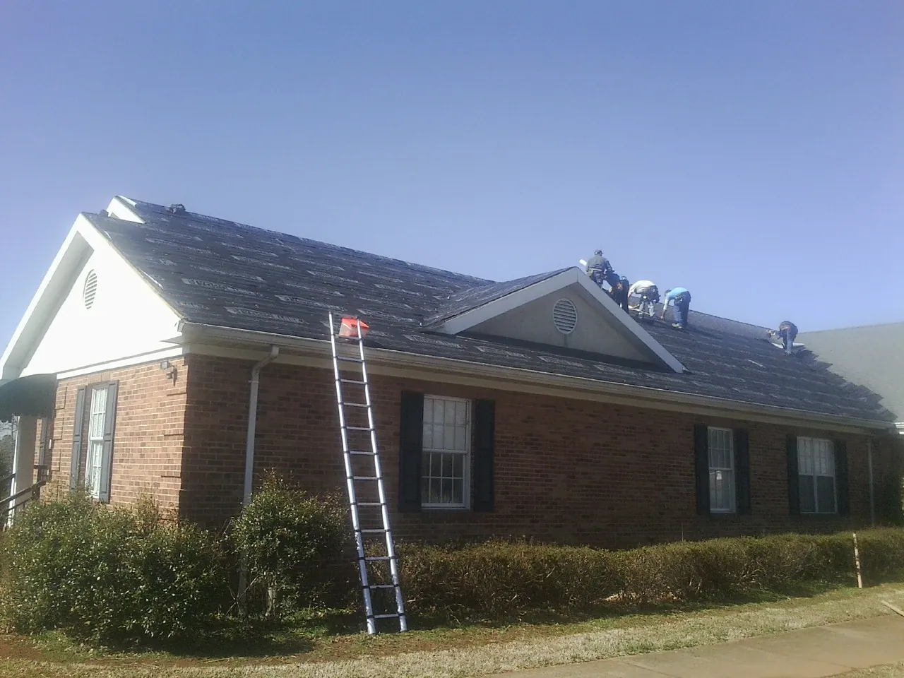 Crew tearing shingles off a brick ranch roof with a ladder set — Metal Roof Repair work by our crew in Mary D