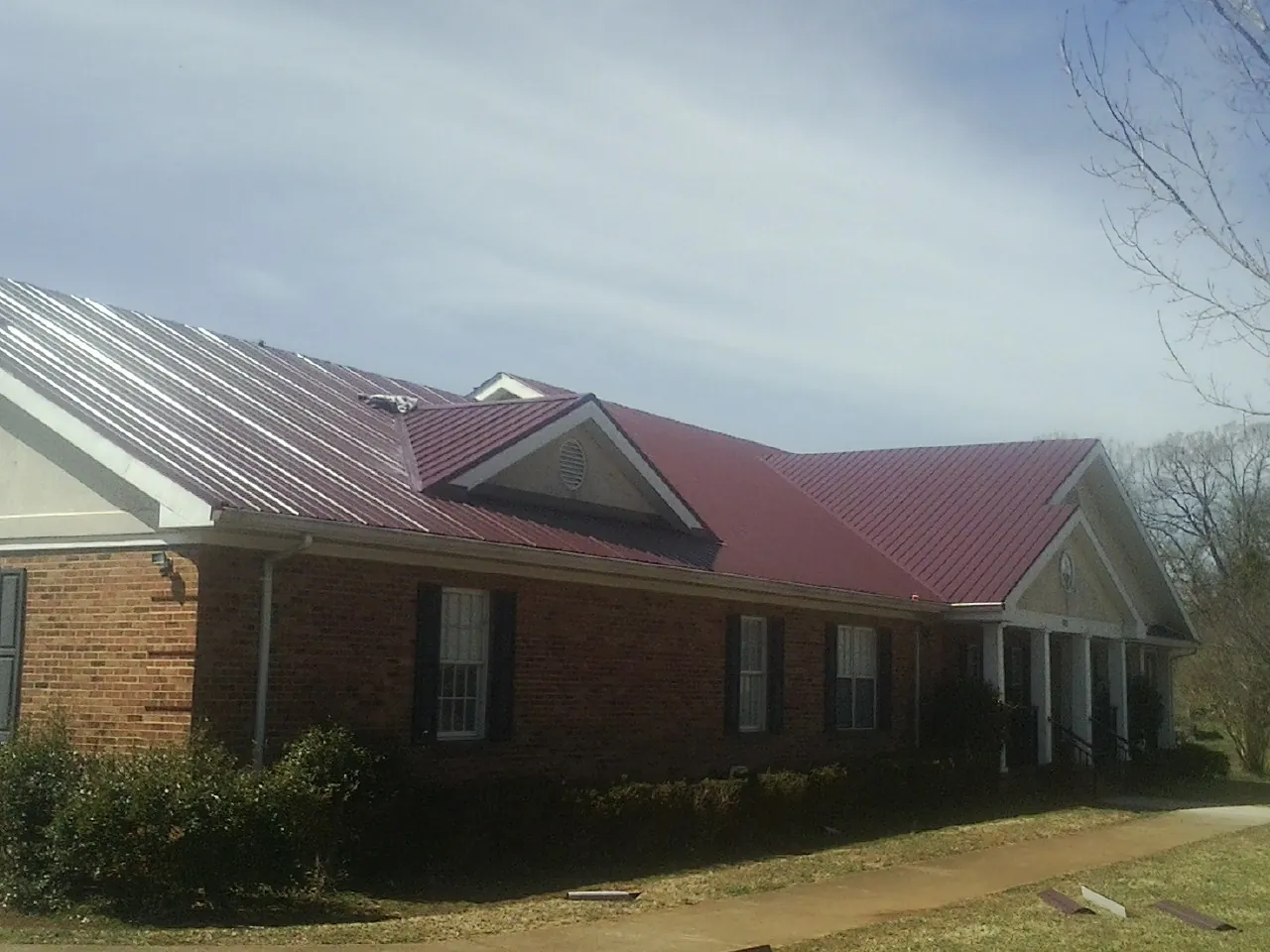 Red metal roof with gabled entries on a long brick building, from a Hail Damage Roof Repair job in Mary D