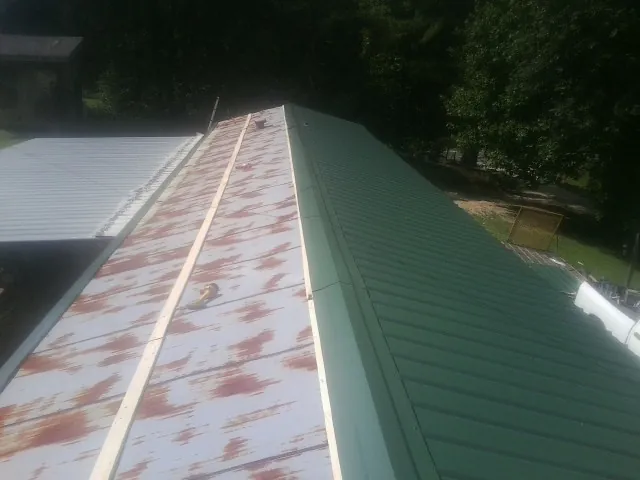 Old rusted panels beside newly installed green metal roofing — Wind Damage Roof Repair by Roofing Brothers in Mary D