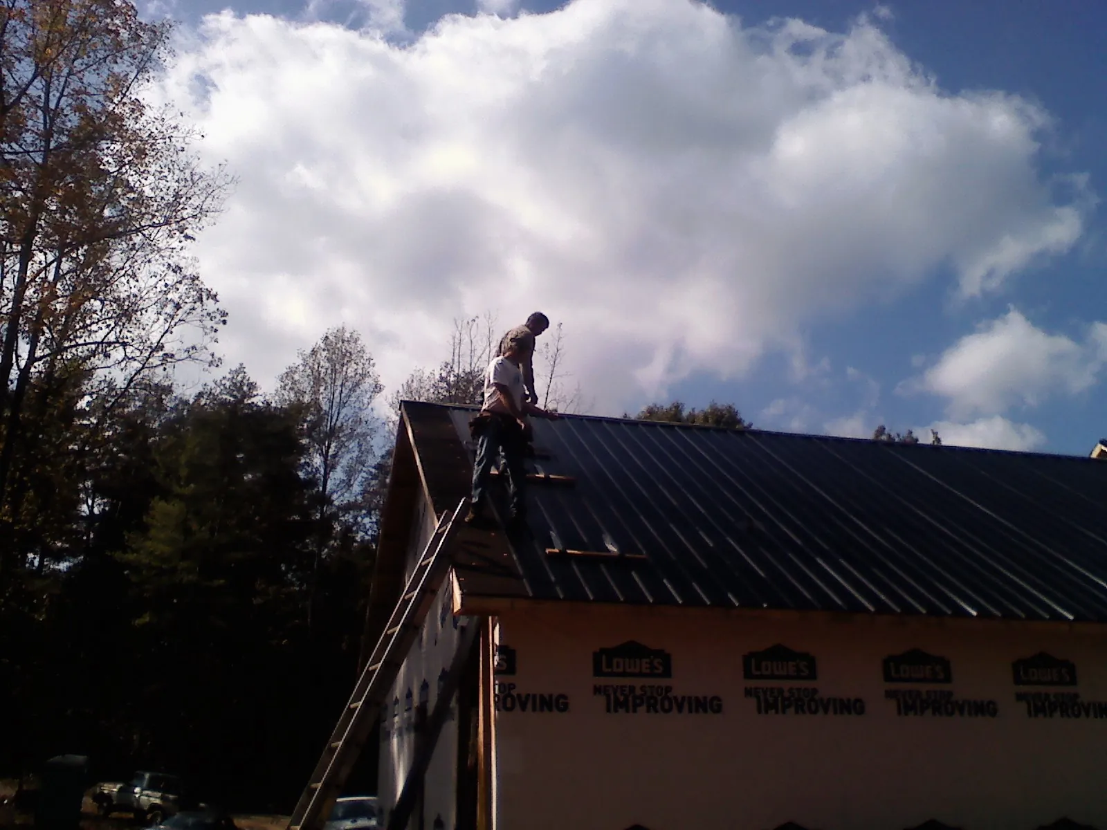 Roofer fastening dark metal panels high against a cloudy sky, from a Roof Inspection job in Mary D
