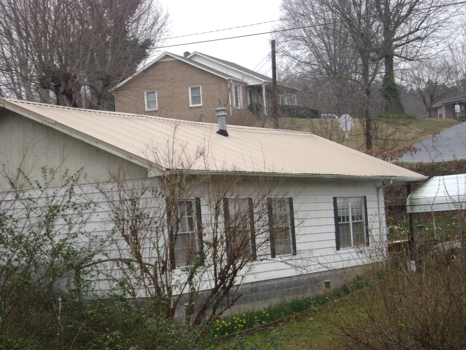 Tan metal roof on a white sided house set into a hillside — Commercial Roofing by Roofing Brothers in Mary D